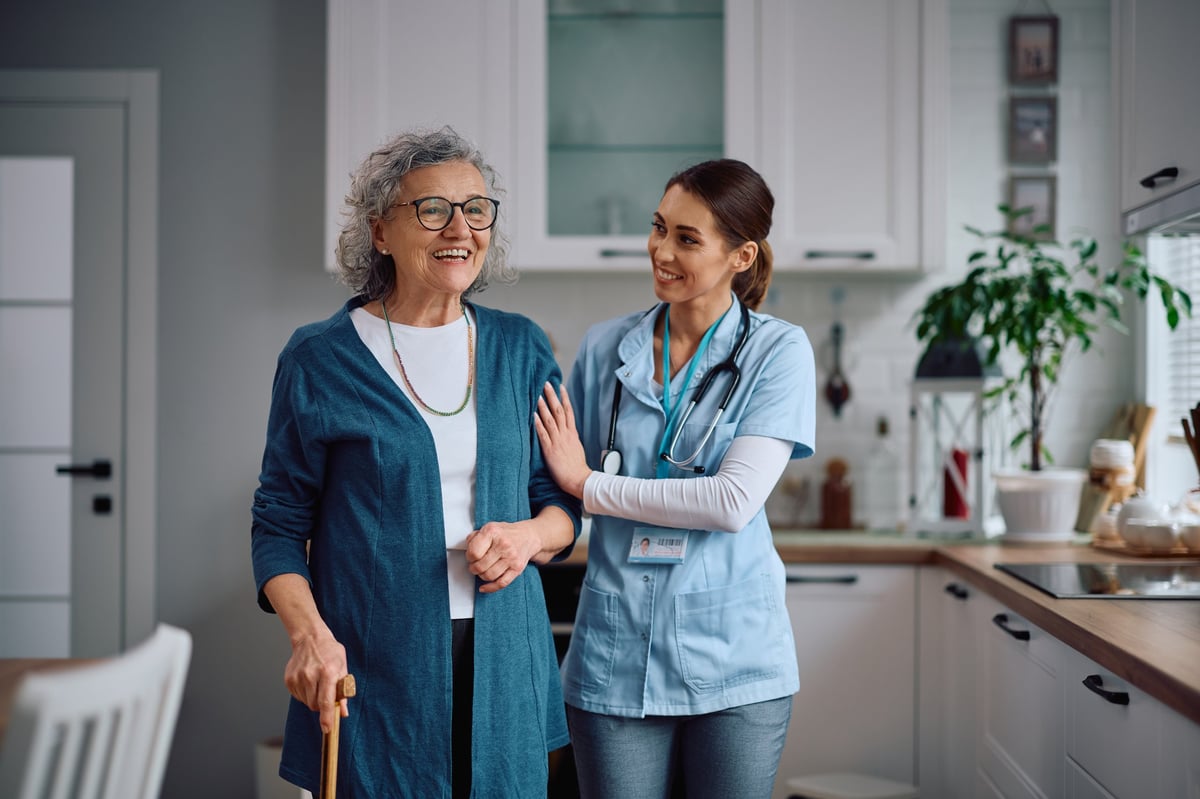 A caring home caregiver assisting a senior while walking through the kitchen