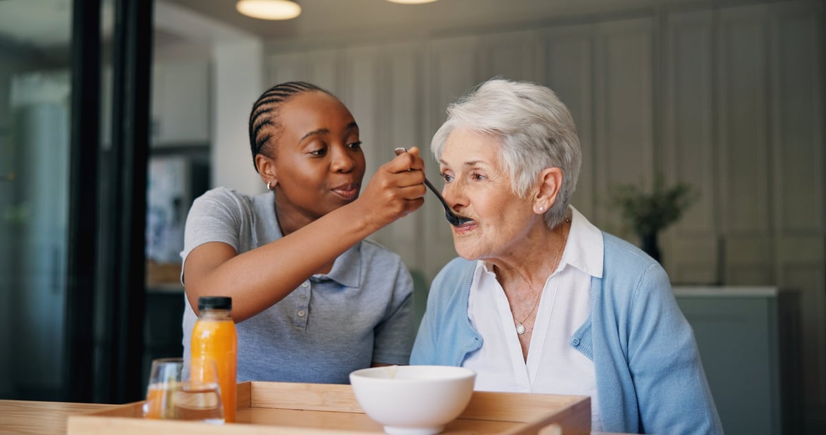 A friendly home caregiver chatting warmly with a smiling senior in a bright living room